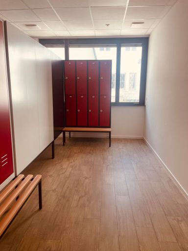 Umkleidekabinen Ein Raum mit abschließbaren roten Schränken und zwei Holzbänken.