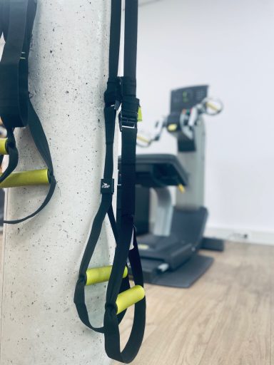 TRX-Training TRX-Bänder an einem Pfosten mit Fitnessgerät im Hintergrund.
