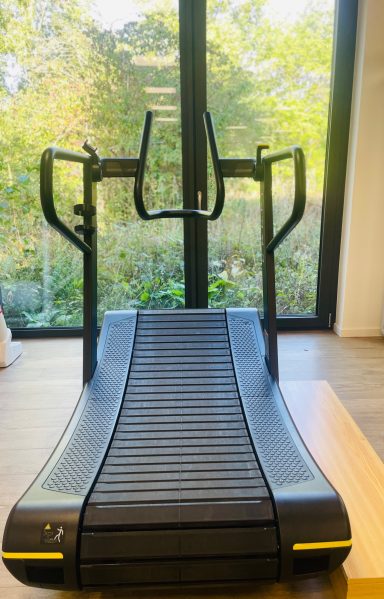 Trainieren mit Blick in den Garten Laufband mit geschwungener Lauffläche, Blick auf Garten durch Fenster.