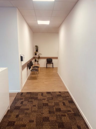 Wartebereich Langer Flur mit Holzfußboden, weißen Wänden und einem Tisch mit Stühlen an der Wand.