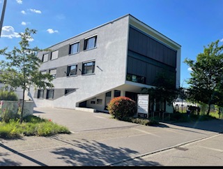 Hier sind wir! Moderner, zweigeschossiger Bürogebäude mit begrüntem Außenbereich und klarem blauen Himmel.