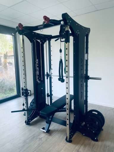 Multipress Fitnessgerät mit Gewichten und verstellbarer Bank in einem hellen Raum platziert.