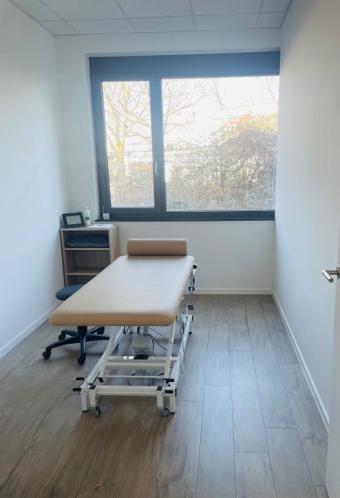 Behandlungszimmer Behandlungsraum mit einer Liege, einem Stuhl und einem Fenster mit Blick ins Freie.